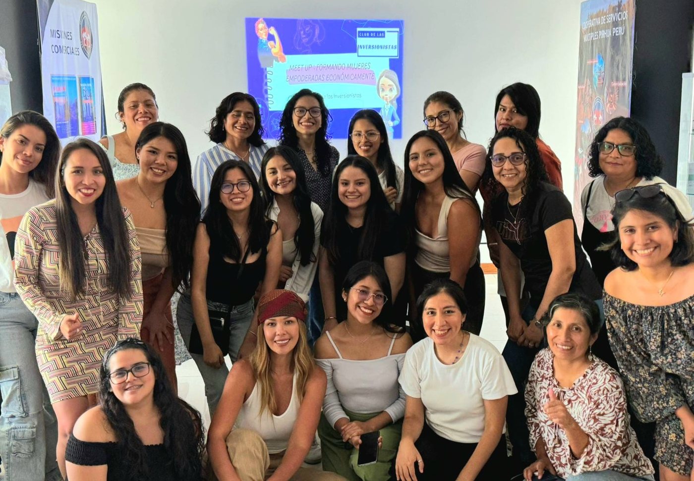 Veinte mujeres reunidas en un meet up sobre independencia económica, con la presentación proyectada al fondo