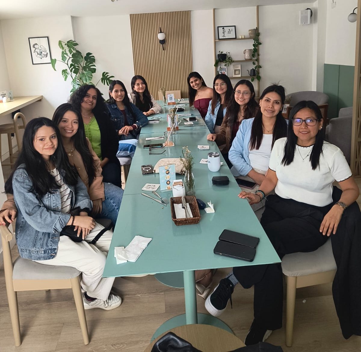 Doce mujeres sentadas a lo largo de una mesa larga en un café de Lima, durante un taller de la comunidad